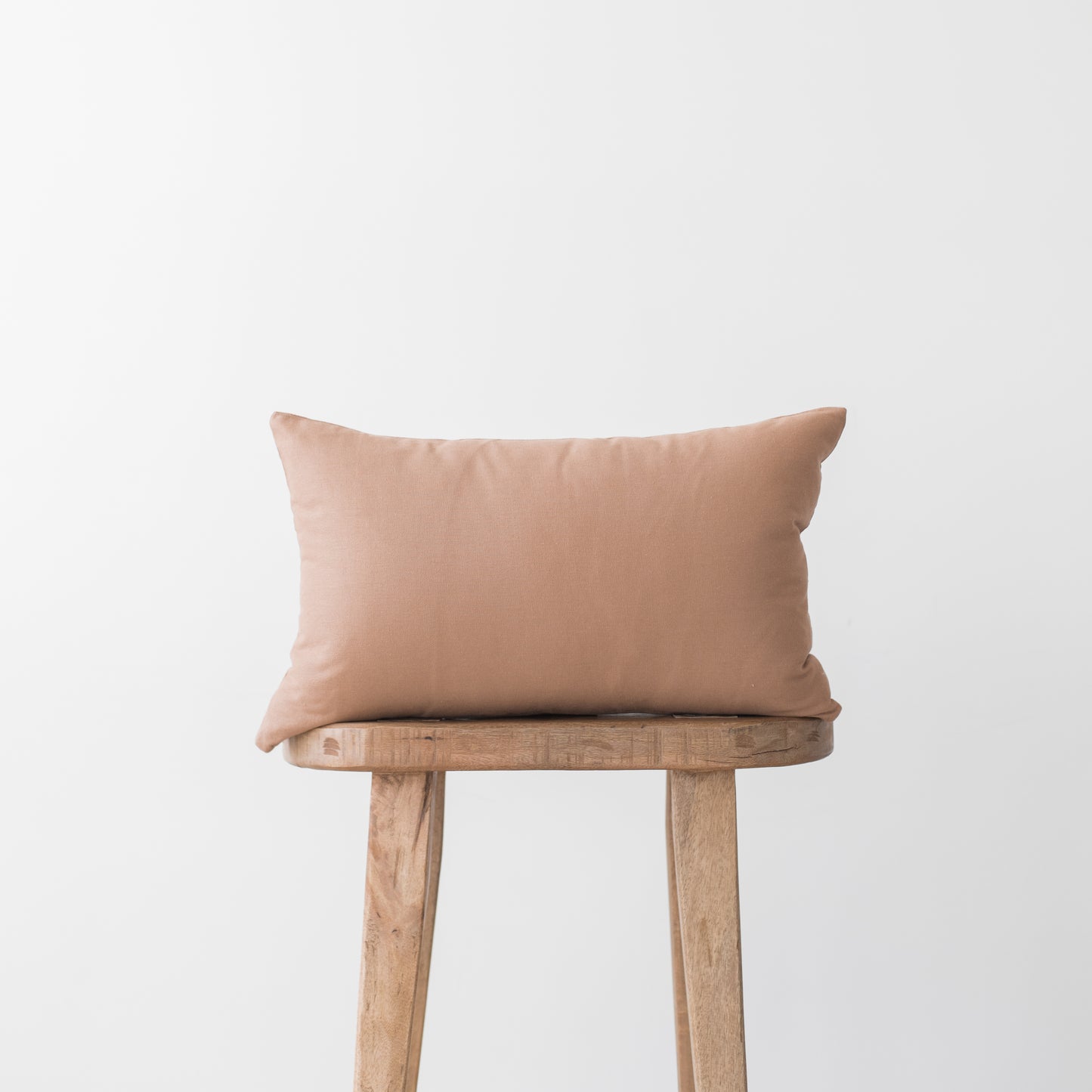 Dusty rose rectangular pillow with solid fabric placed on wooden stool.