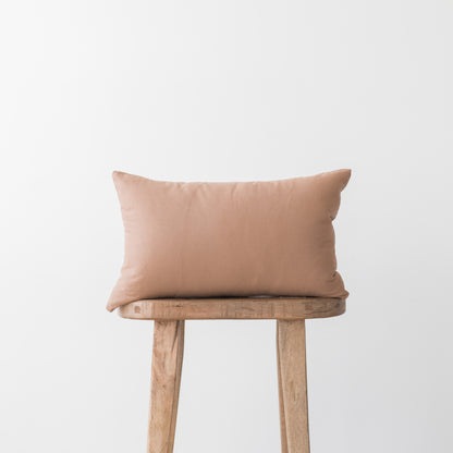 Dusty rose rectangular pillow with solid fabric placed on wooden stool.