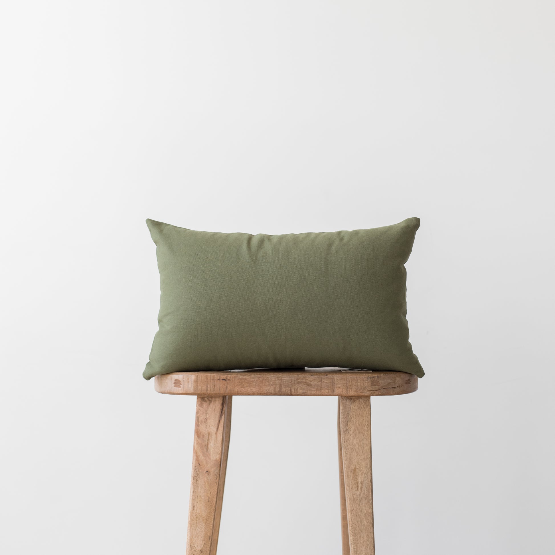 Olive green rectangular pillow placed on a wooden stool against a white background.