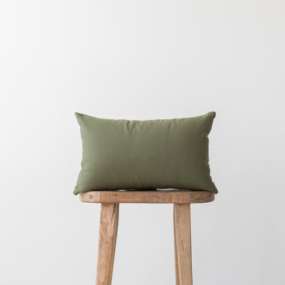Olive green rectangular pillow placed on a wooden stool against a white background.
