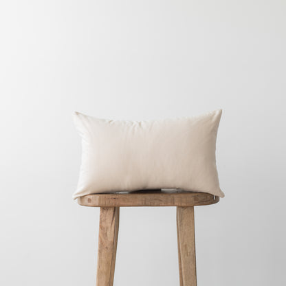 Cream-colored rectangular pillow with smooth fabric displayed on a wooden stool.