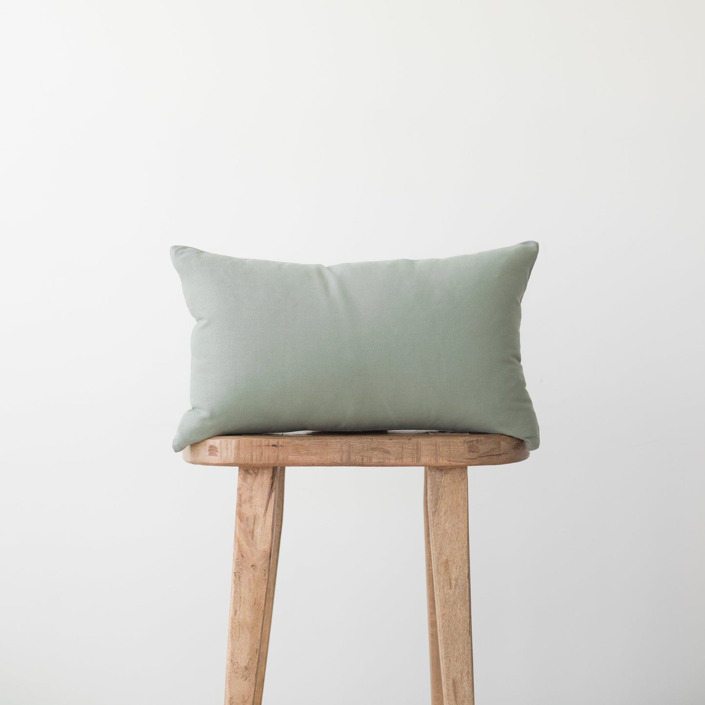 Sage green rectangular pillow with solid woven fabric displayed on wooden stool.
