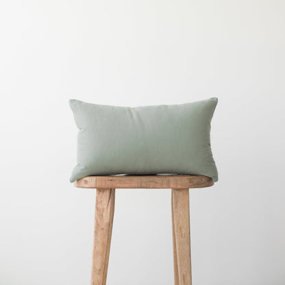 Sage green rectangular pillow with solid woven fabric displayed on wooden stool.