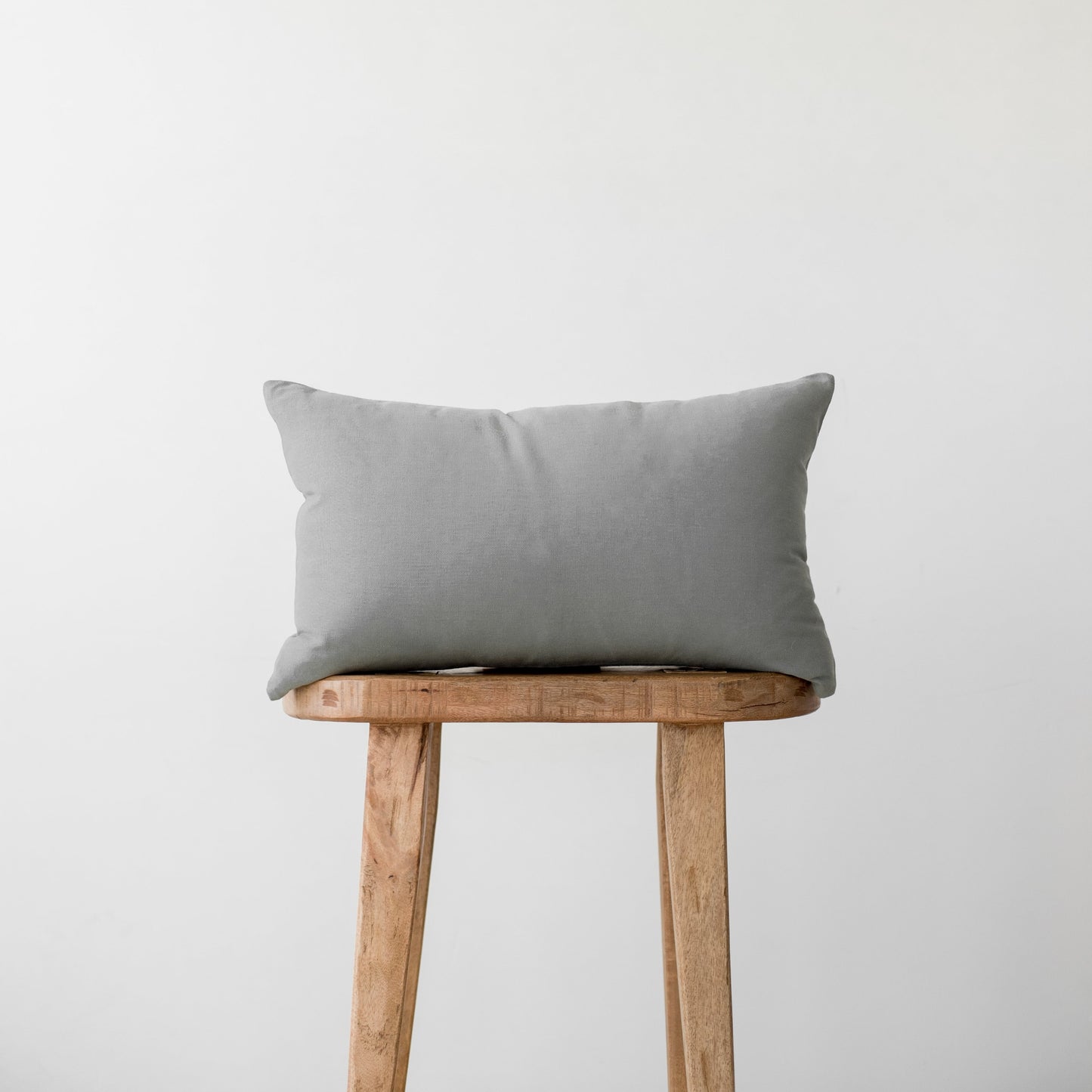 Gray linen pillow with corner ties resting on a wooden stool.