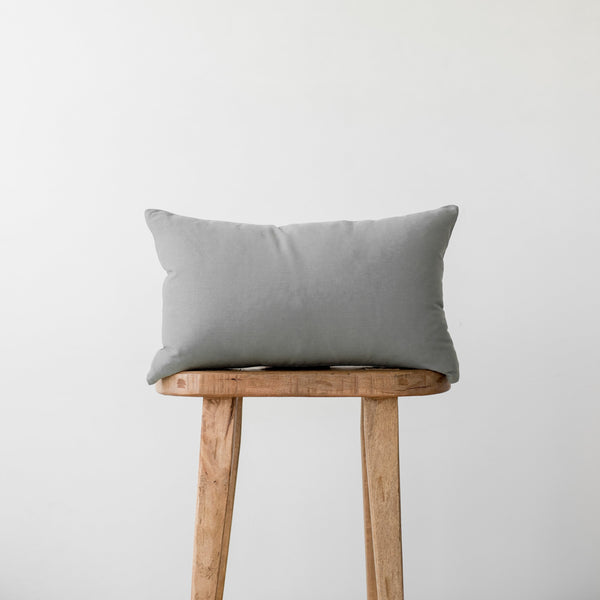 Gray linen pillow with corner ties resting on a wooden stool.