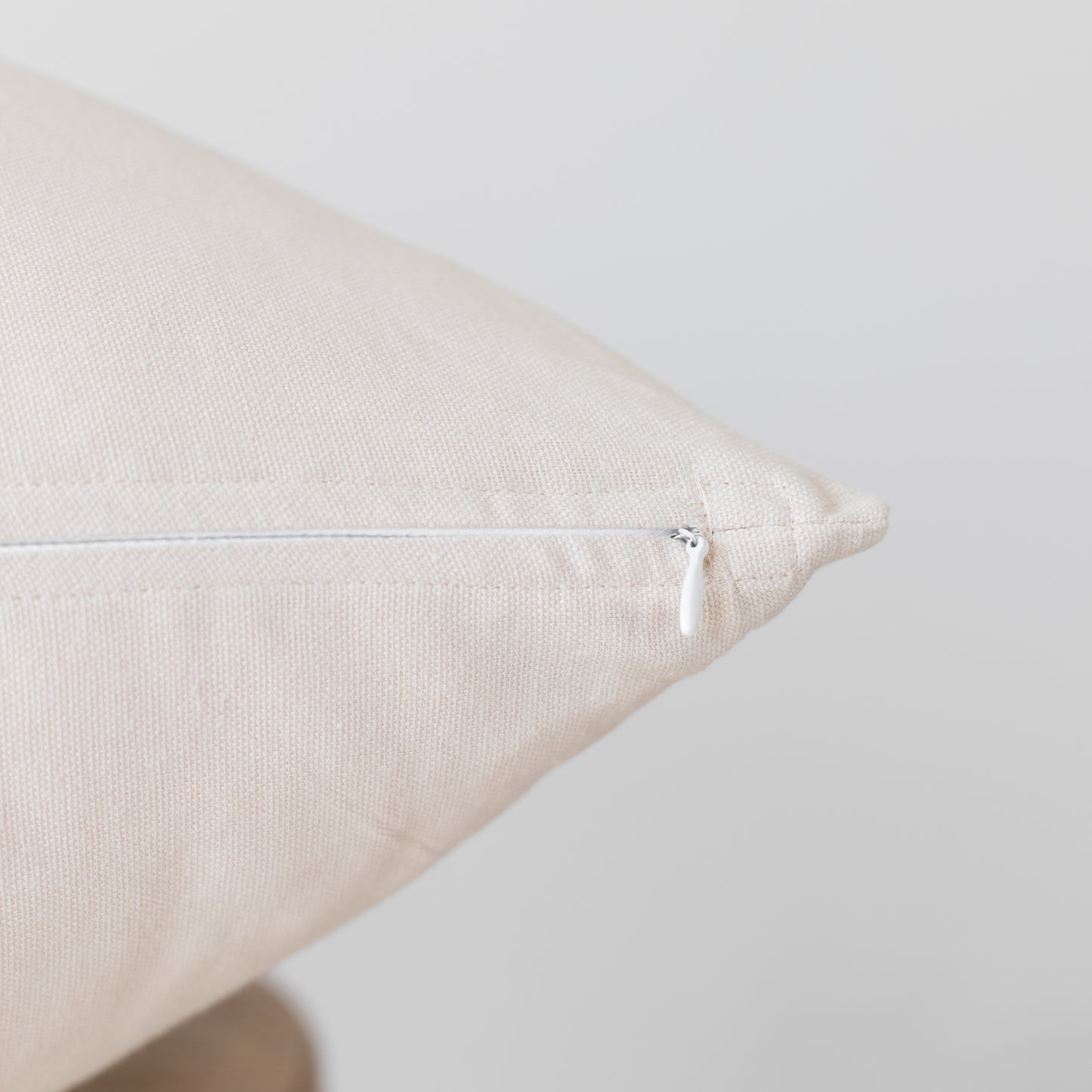 Beige linen pillow with white zipper closure shown at an angle.