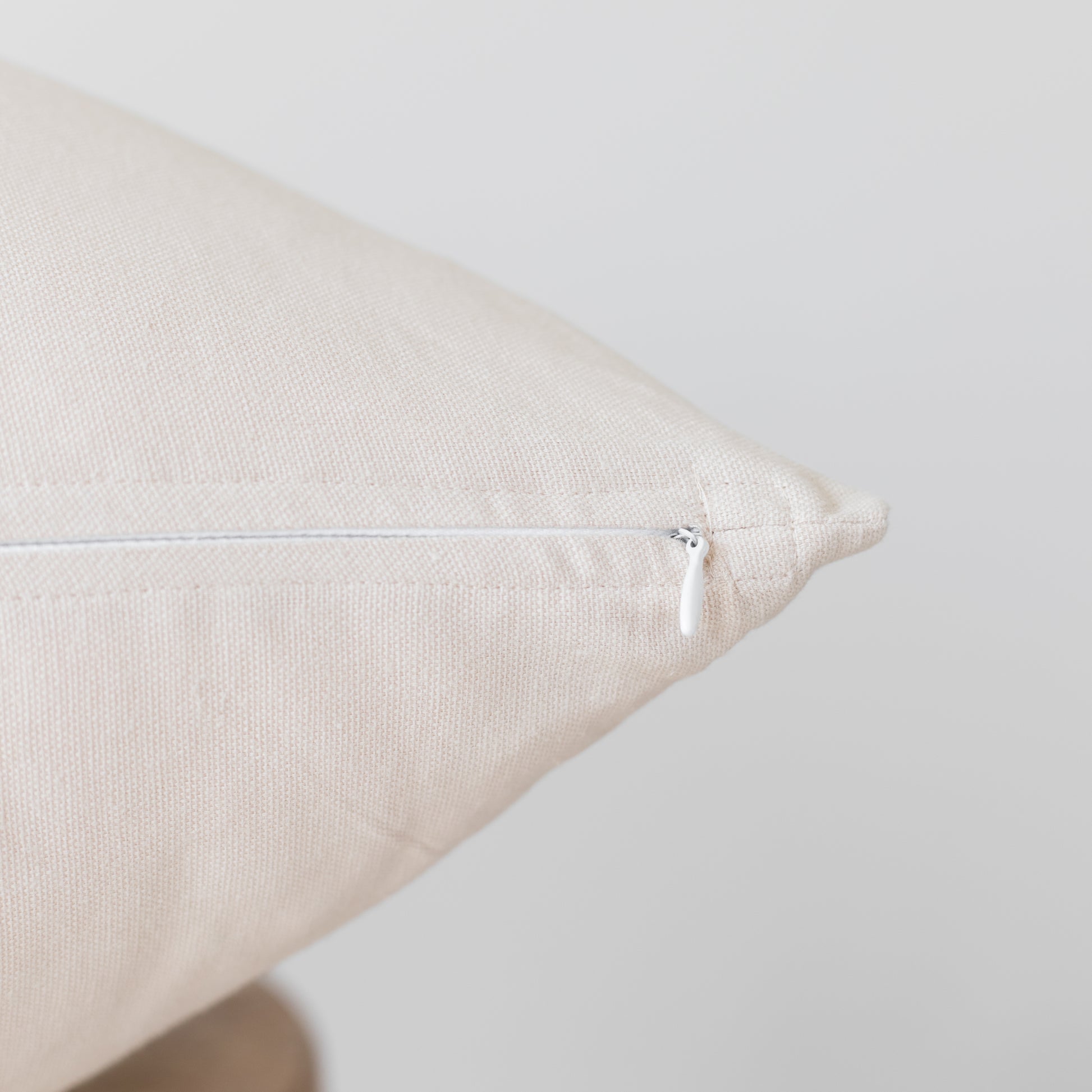 Beige linen pillow with white zipper closure shown at an angle.