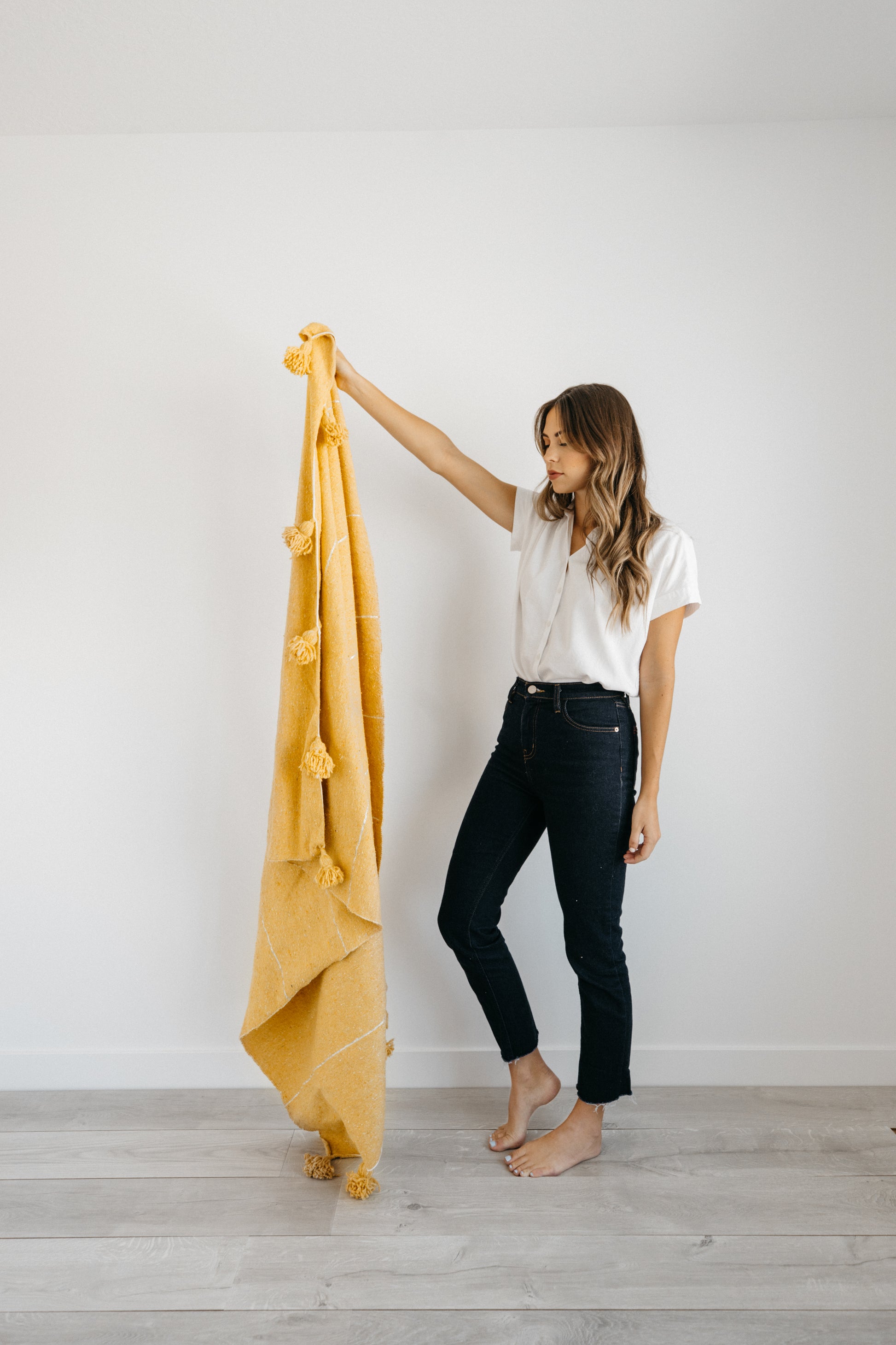 Yellow throw blanket with tassel corners held up by woman wearing white tee and dark jeans.