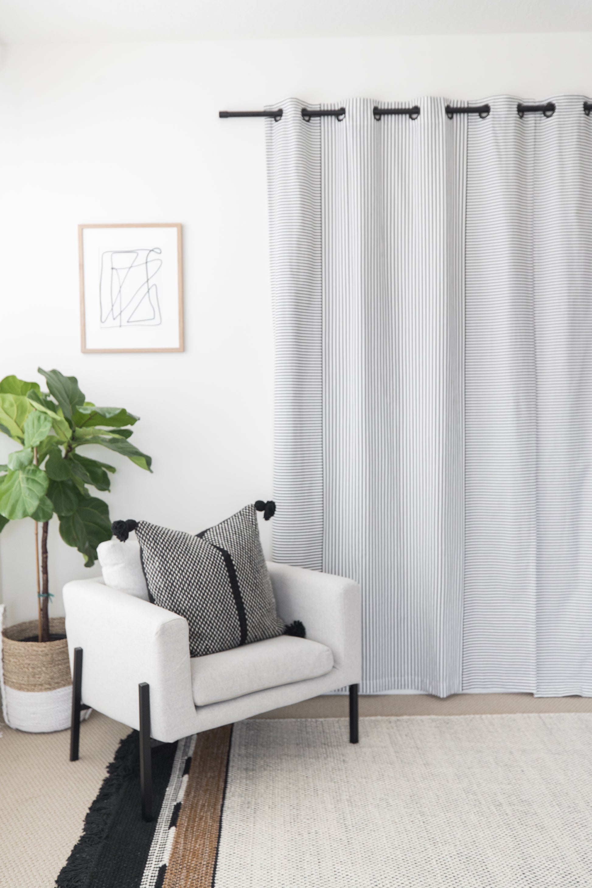 Two white curtain panels with gray vertical stripes and grommet top rings hung on a black rod.