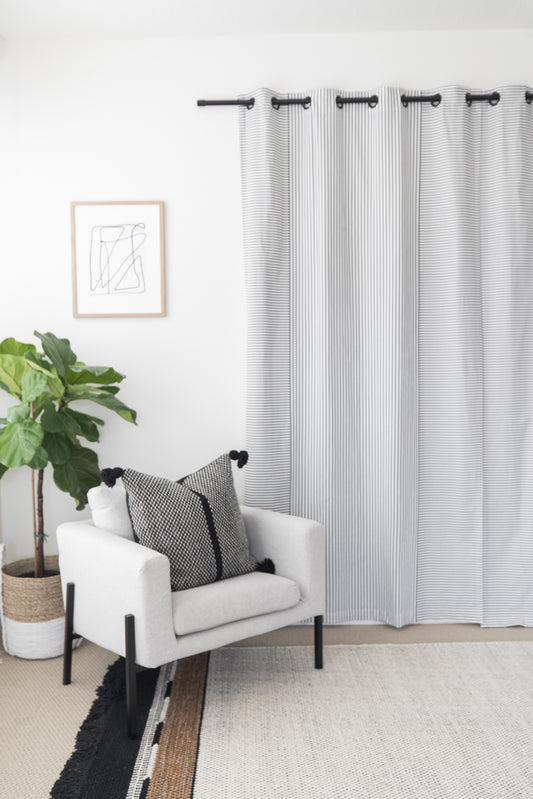 Two white curtain panels with gray vertical stripes and grommet top rings hung on a black rod.