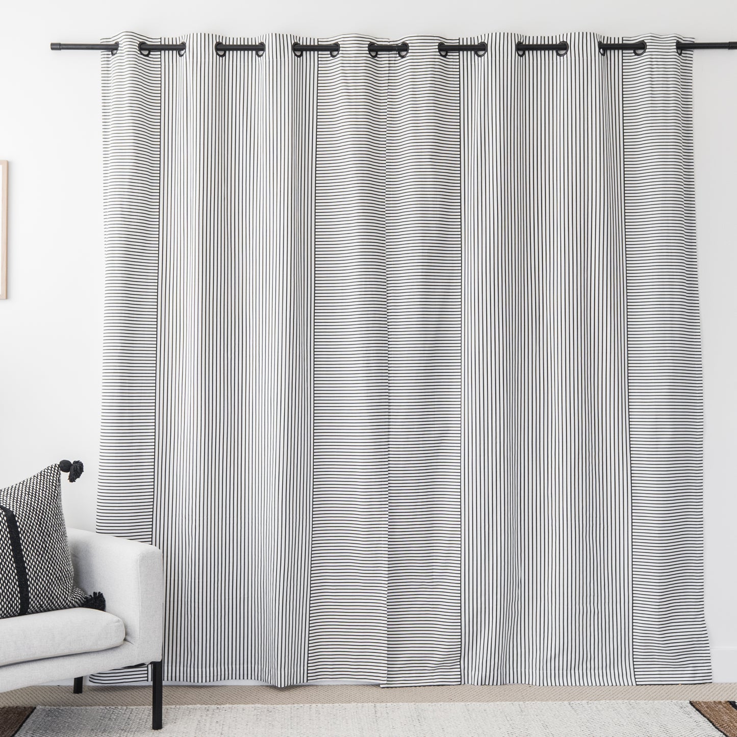 Two white curtain panels with fine black vertical stripes and grommet tops hanging on a black rod.