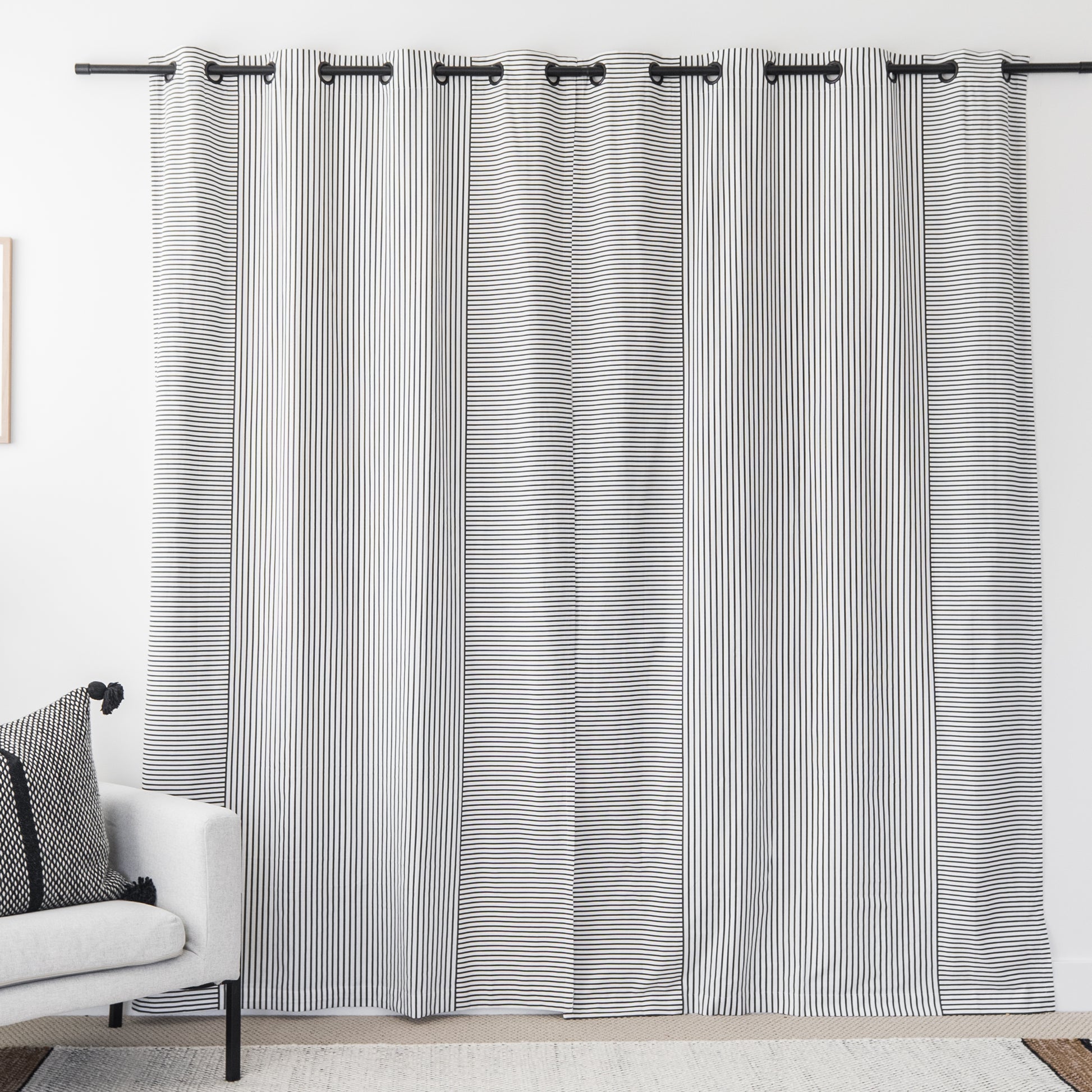 Two white curtain panels with fine black vertical stripes and grommet tops hanging on a black rod.