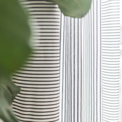 Two white curtain panels with horizontal gray and black stripes hanging against a green background.