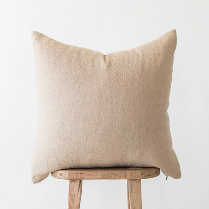 Beige linen pillow cover with envelope closure displayed on wooden chair back.