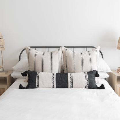 Bed with striped cream and charcoal pillows with black tassels arranged against a metal headboard.