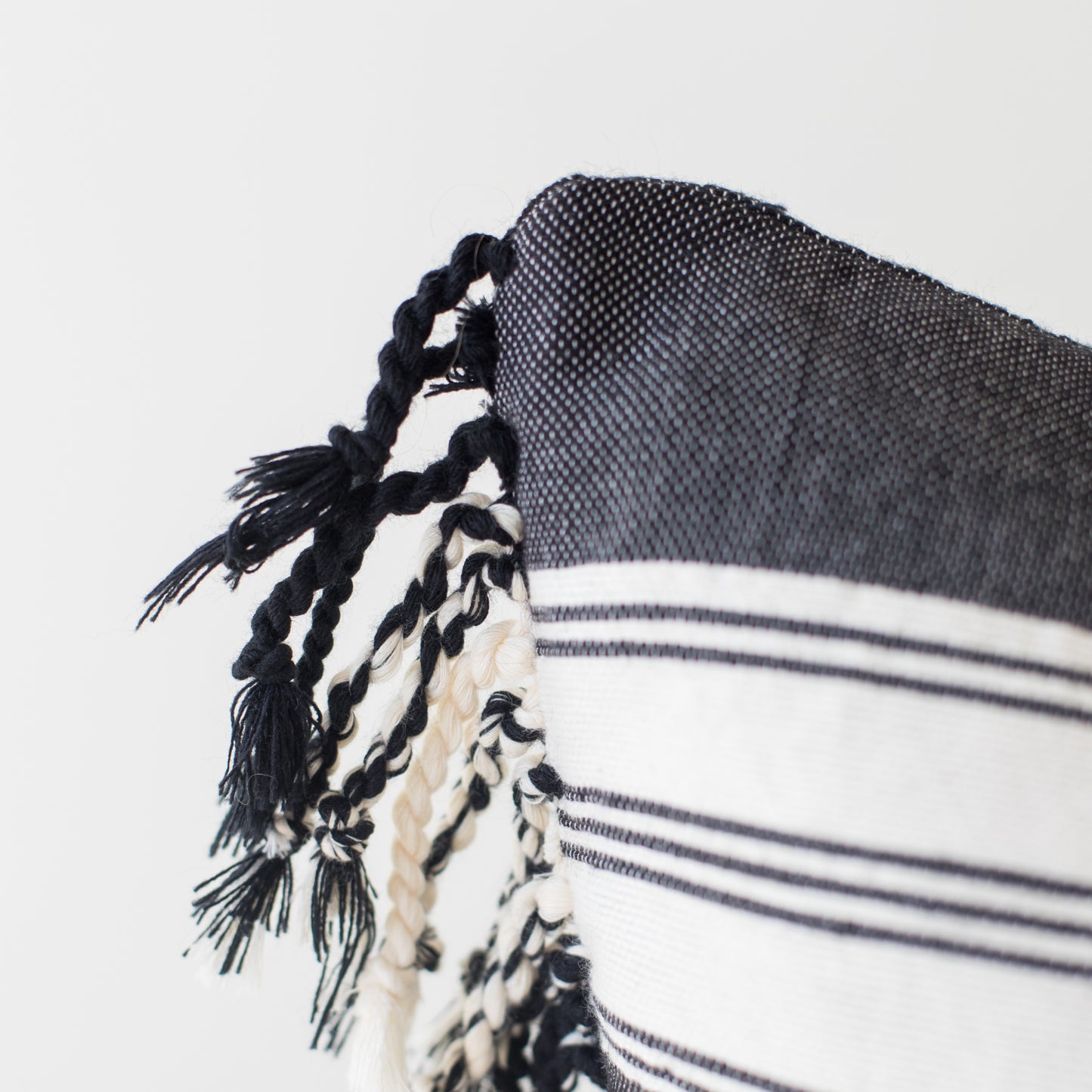 Dark woven throw with white striped pattern and black twisted fringe trim along edge.