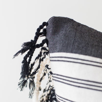 Dark woven throw with white striped pattern and black twisted fringe trim along edge.