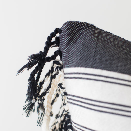 Dark woven throw with white striped pattern and black twisted fringe trim along edge.