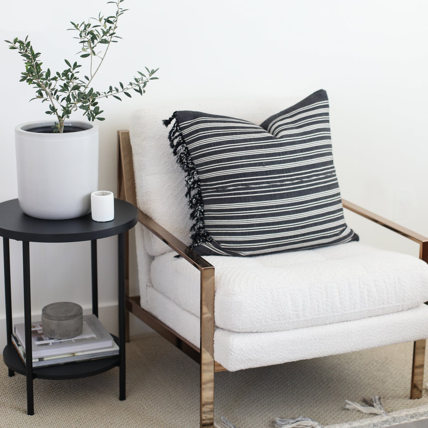 Black and white striped pillow with fringe trim on natural wood-frame chair with cream cushion.