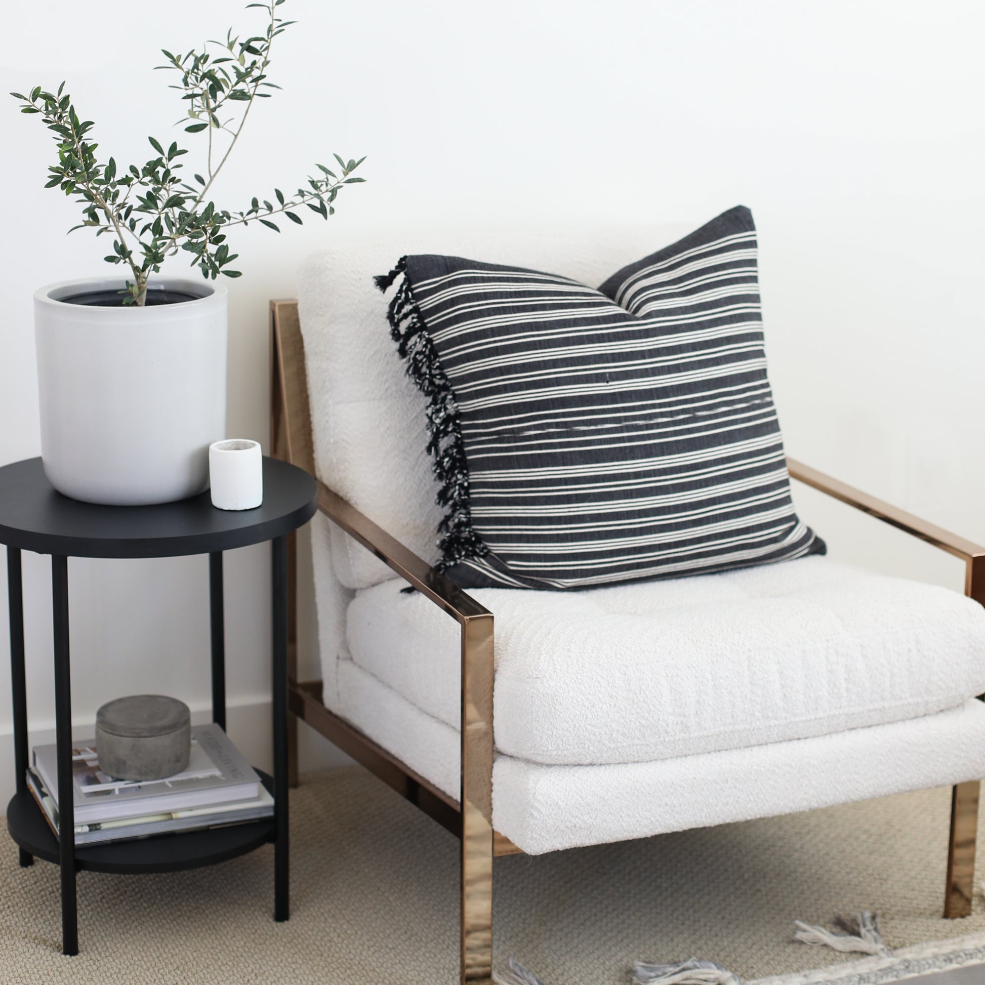 Black and white striped pillow with fringe trim on natural wood-frame chair with cream cushion.