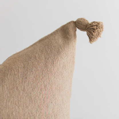 Beige knit pillow with textured surface and tassel detail at corner.