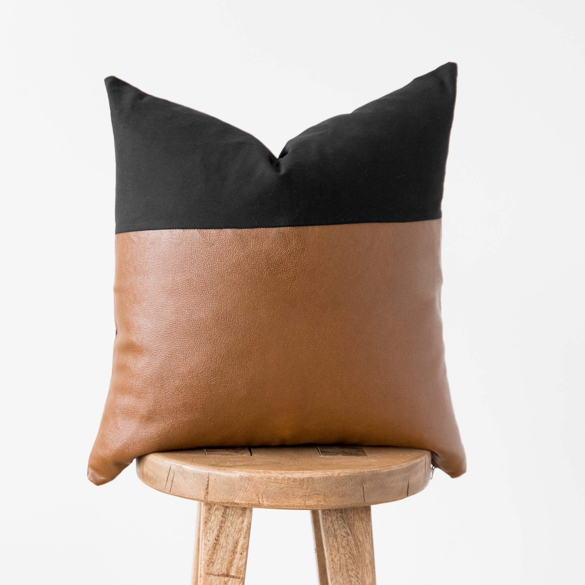 Black and tan two-tone cushion cover with pointed corners, displayed on a wooden stool.