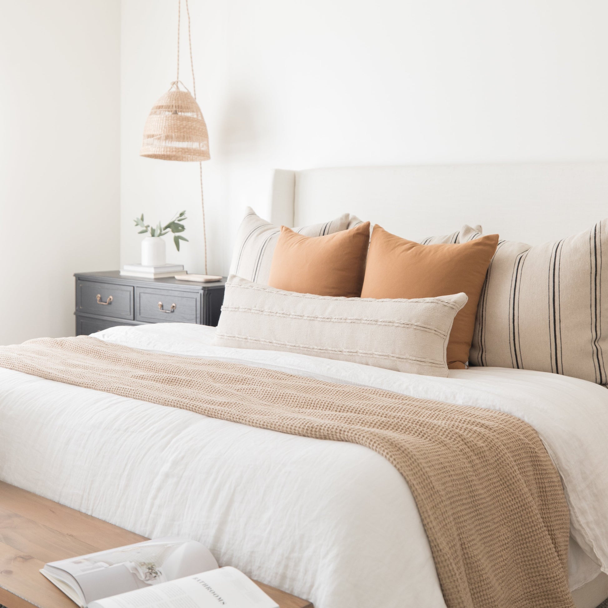Terracotta-colored throw pillows arranged on a bed with white bedding and a tan woven throw.