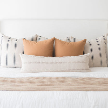 Terracotta and cream throw pillows arranged on a bed with striped and textured bedding.
