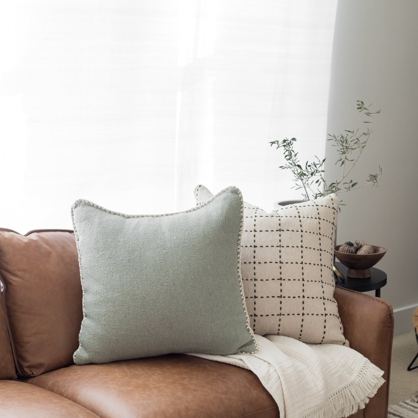 Light green textured pillow with frayed edges displayed on a brown leather chair.