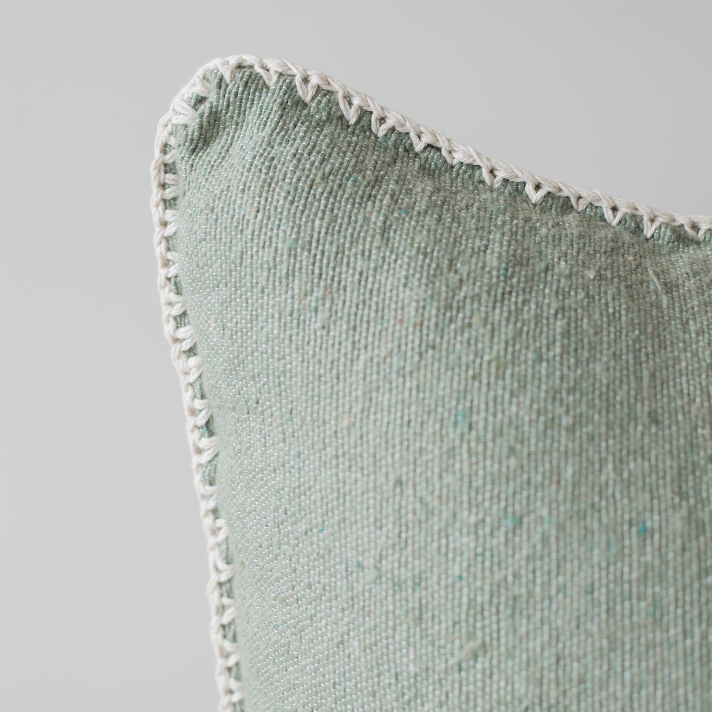 Sage green textured throw pillow with white whipstitched edge detail and ribbed fabric surface.