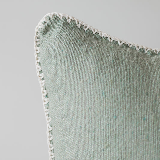 Sage green textured throw pillow with white whipstitched edge detail and ribbed fabric surface.