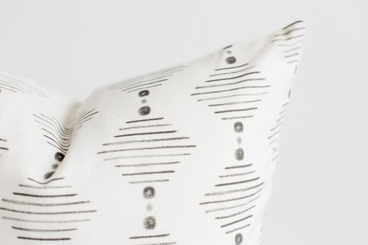 Four white pillows with gray horizontal lines and circular dot patterns arranged in a stack.