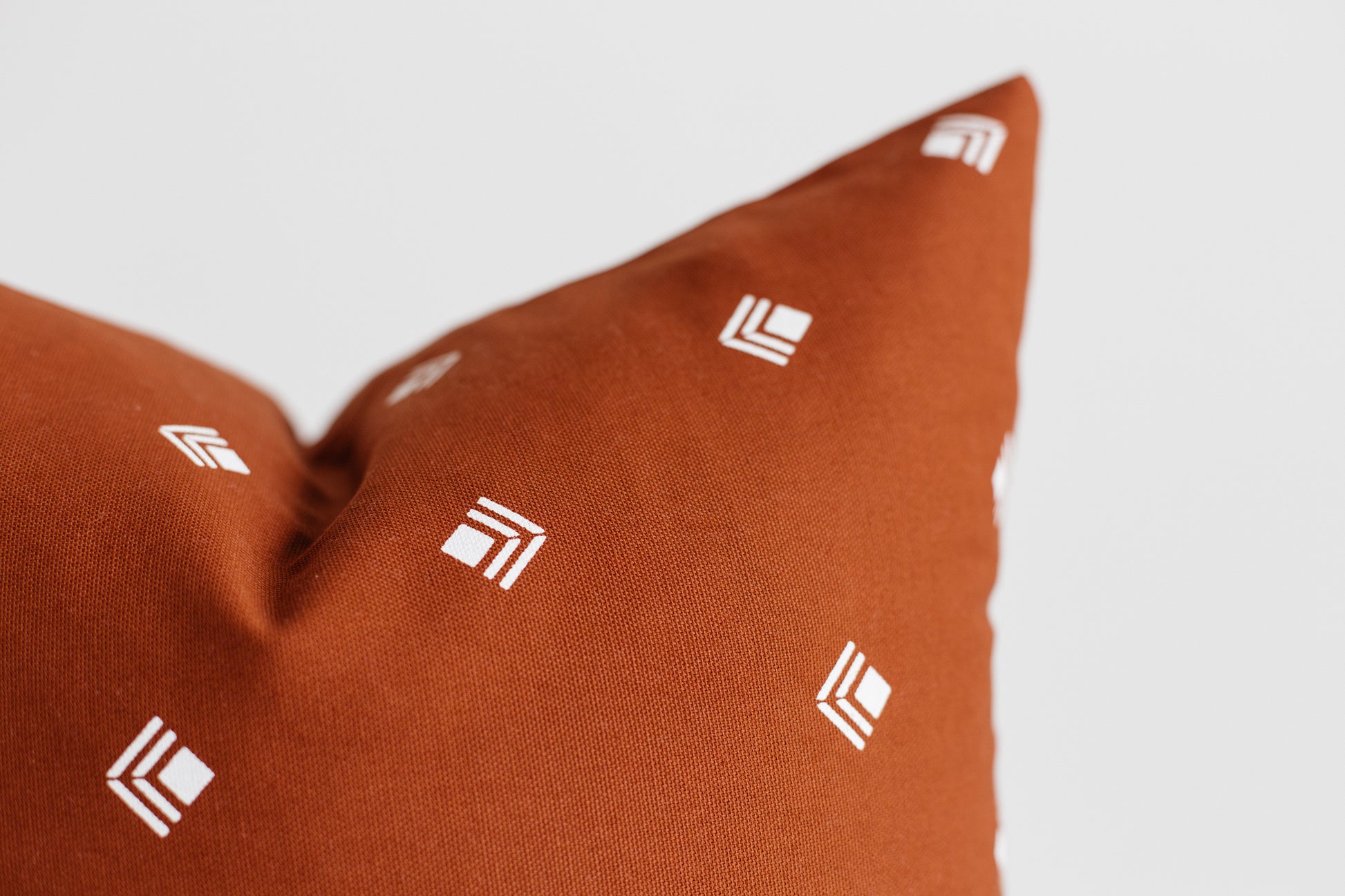 Rust-colored pillow with white geometric logo pattern scattered across fabric surface.
