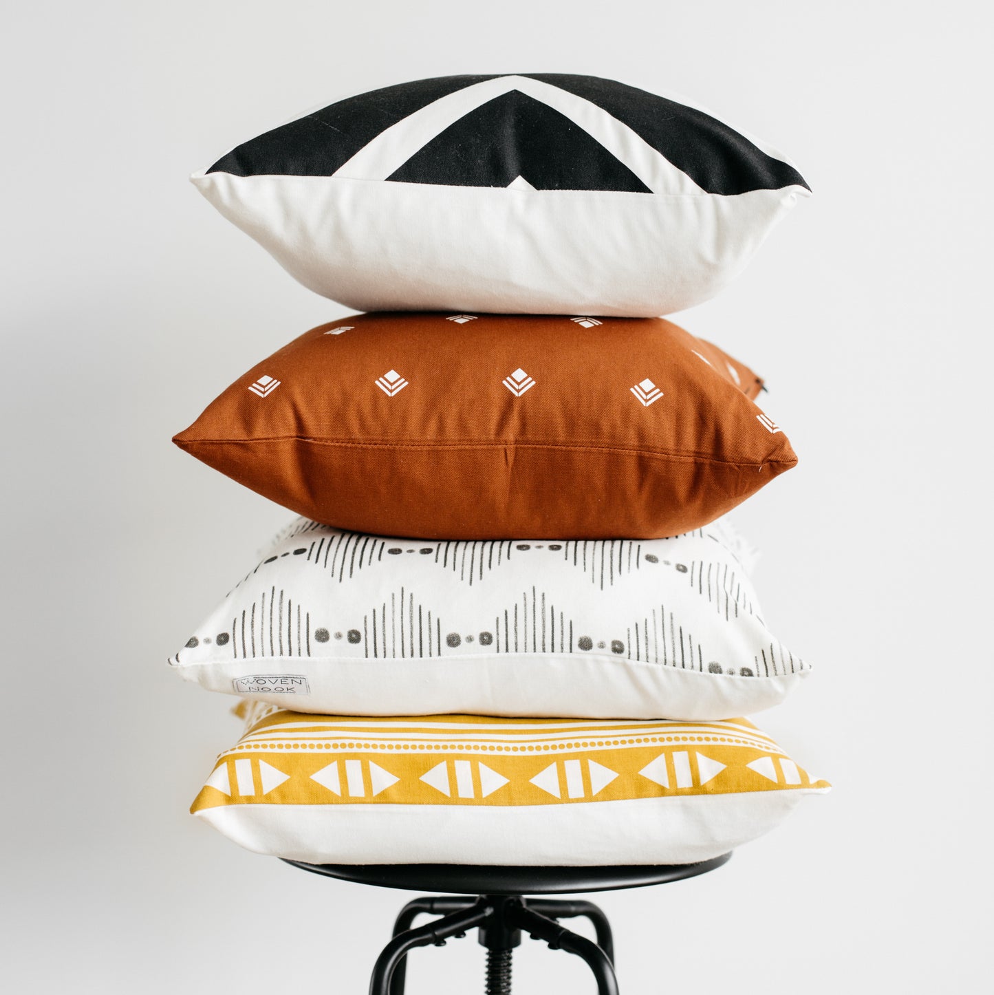 Four 18-inch pillows stacked in black and white geometric, rust with embroidered diamonds, cream with gray patterns, and gold