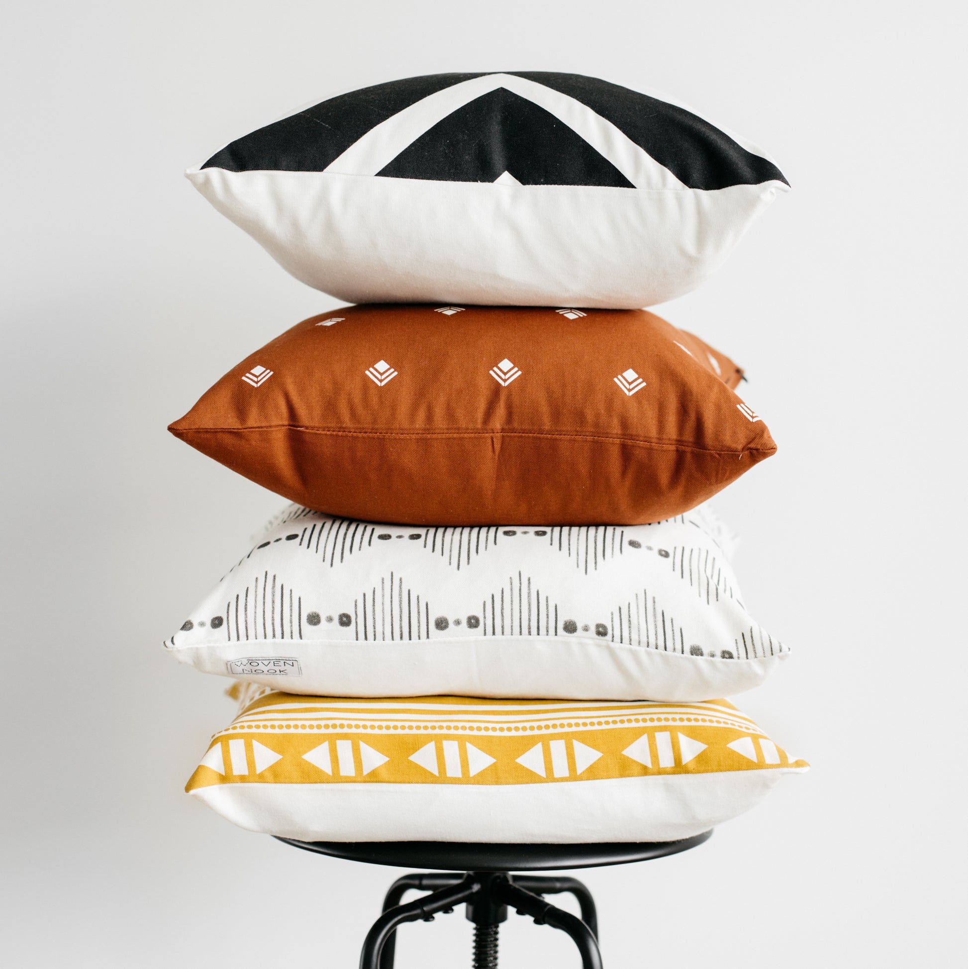Four 18-inch pillows stacked in black and white geometric, rust with embroidered diamonds, cream with gray patterns, and gold