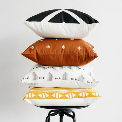 Four 18-inch pillows stacked in black and white geometric, rust with embroidered diamonds, cream with gray patterns, and gold