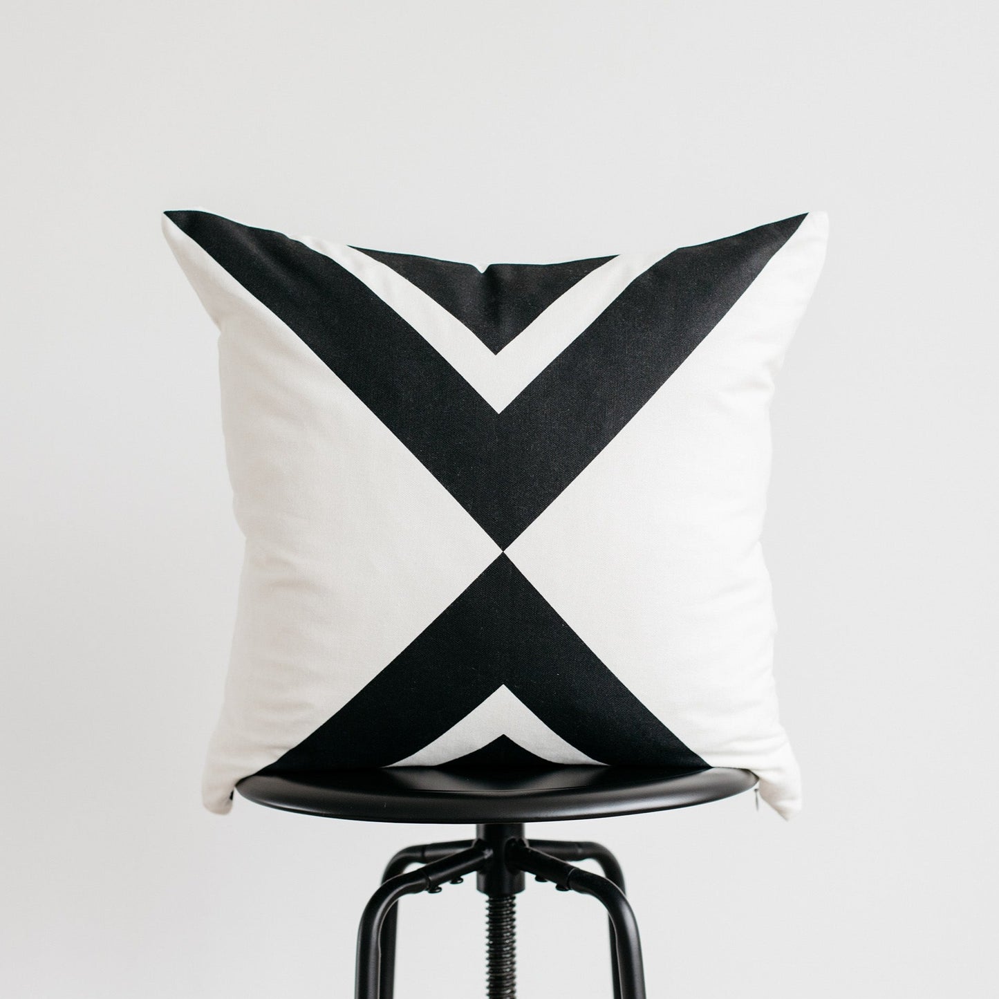 White and black geometric patterned pillow displayed on a black industrial stool.