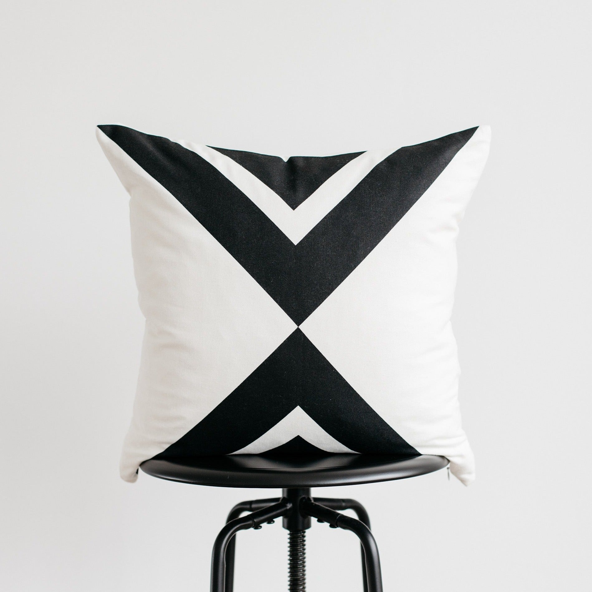 White and black geometric patterned pillow displayed on a black industrial stool.