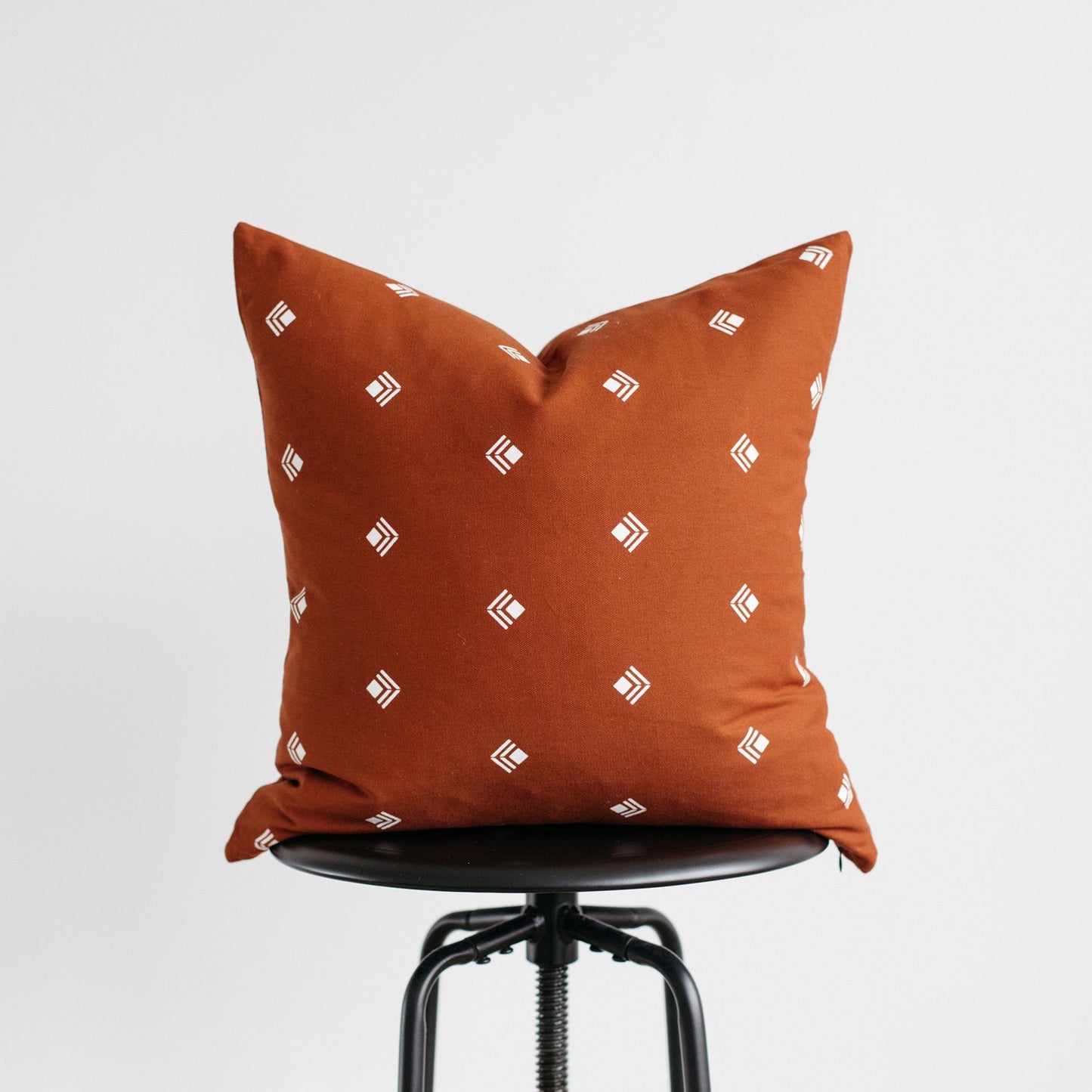 Rust-orange pillow with white geometric pattern displayed on black chair seat.