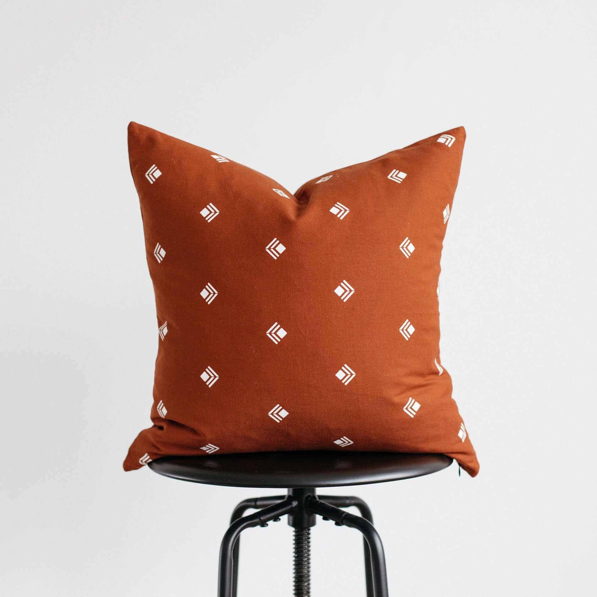 Rust-orange pillow with white geometric pattern displayed on black chair seat.