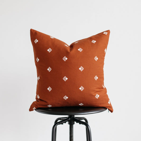 Rust-orange pillow with white geometric pattern displayed on black chair seat.