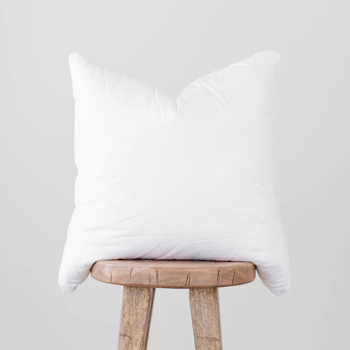 White faux down pillow insert with quilted construction, displayed on a wooden stool.