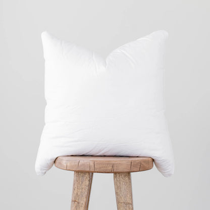White faux down pillow insert with quilted construction, displayed on a wooden stool.
