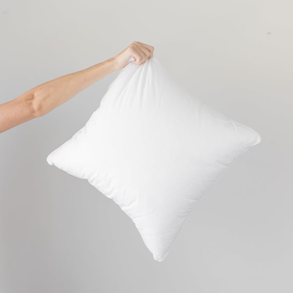 White faux down pillow insert held by hand against neutral background.