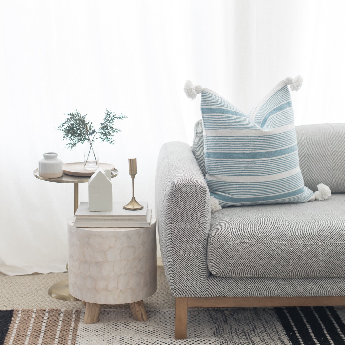 Light gray upholstered sofa with rolled arms and blue striped throw pillow, styled with side tables and decor.