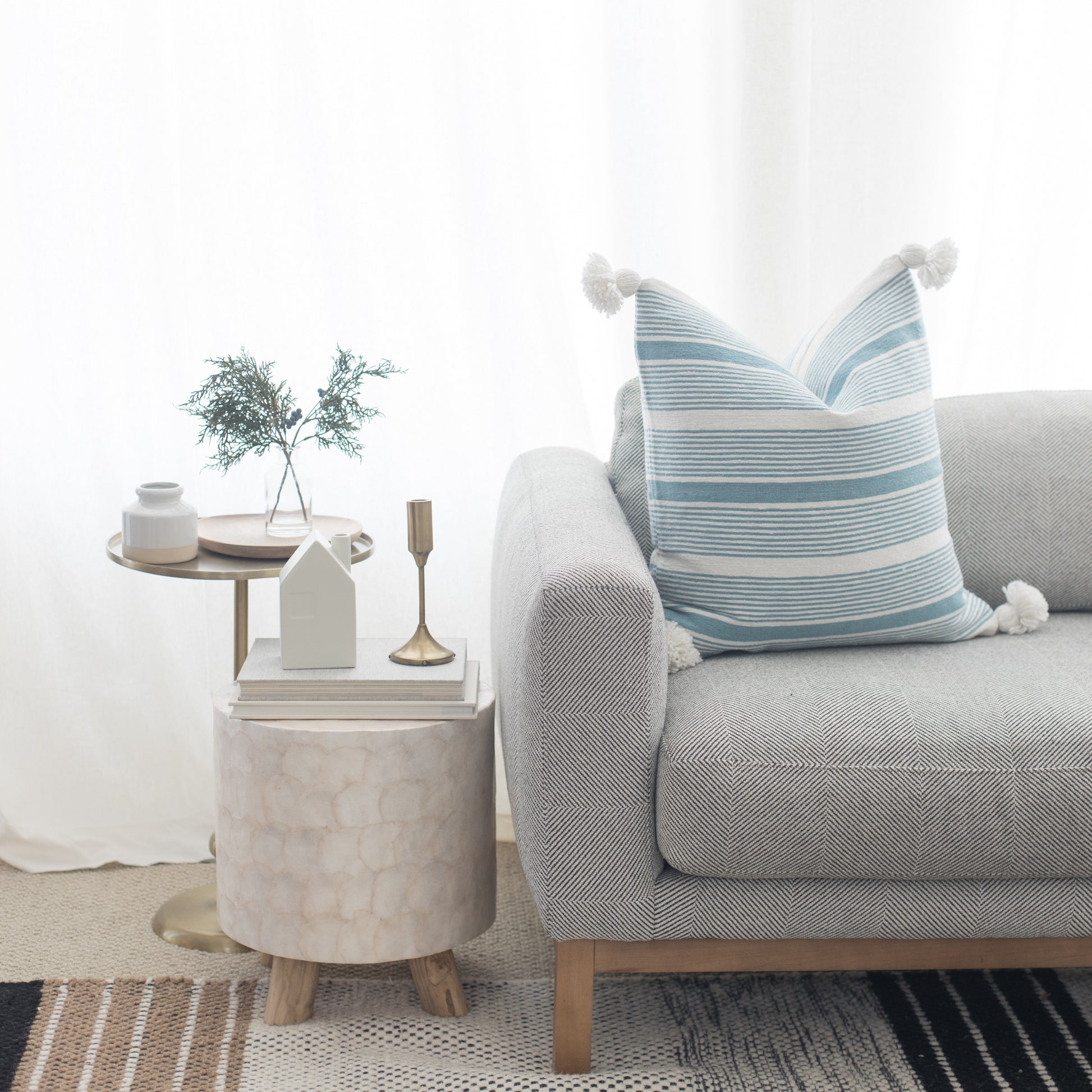 Light gray upholstered sofa with rolled arms and blue striped throw pillow, styled with side tables and decor.