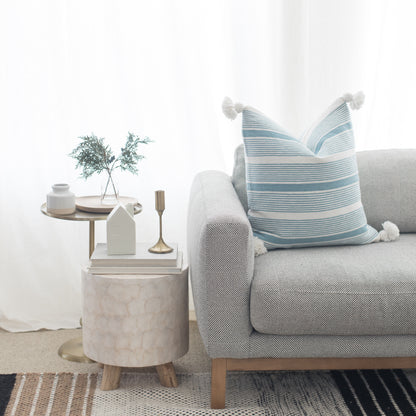 Light gray upholstered sofa with rolled arms and blue striped throw pillow, styled with side tables and decor.