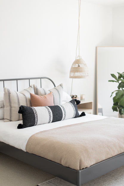 Rectangular lumbar pillow with dark gray and white horizontal stripes and black tassels on a bed.