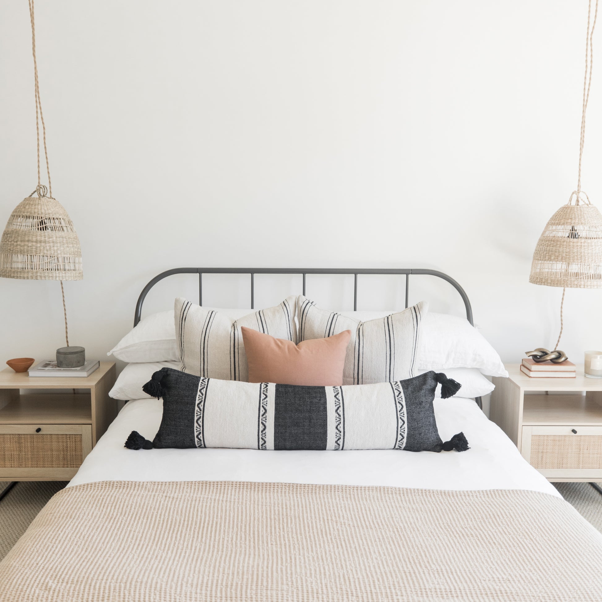 Rectangular lumbar pillow with black and white geometric striped pattern and black tassel corners, displayed on a bed.