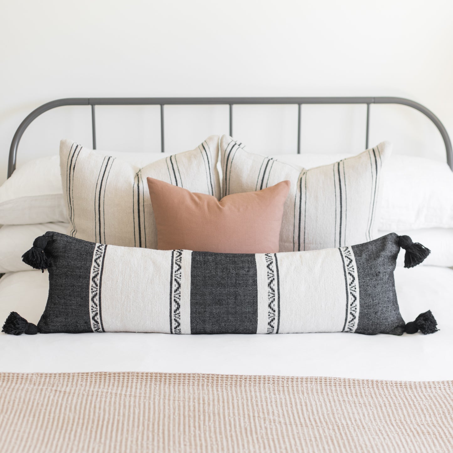 Charcoal and cream striped lumbar pillow with black tassels displayed on a bed with coordinating pillows.